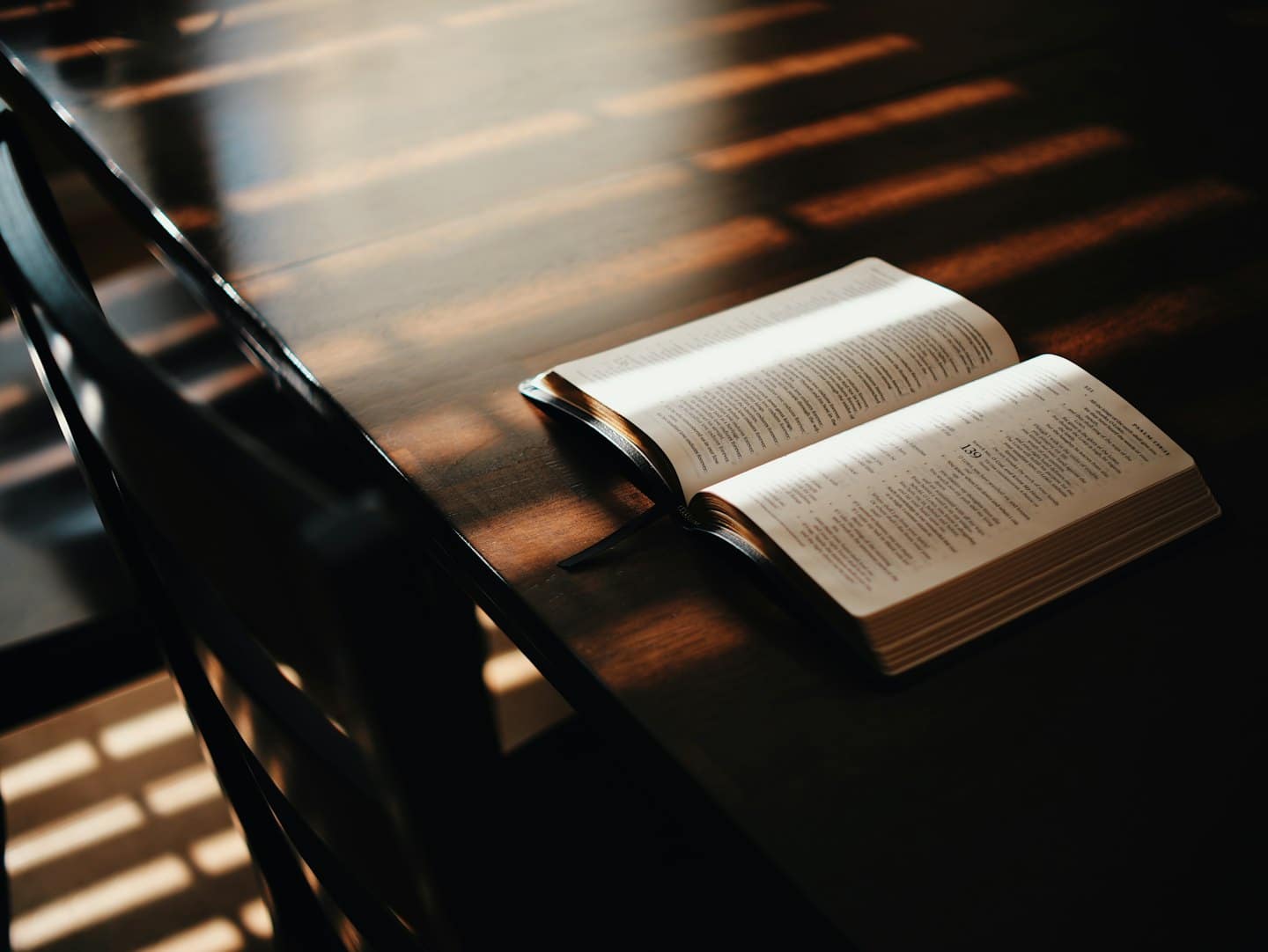 Una Bibbia aperta riposa su un tavolo di legno scuro con la luce del sole sulle pagine.