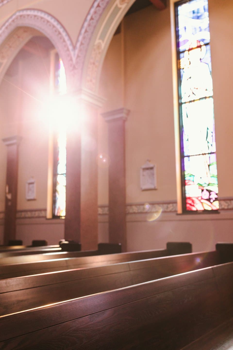 La luce del sole filtra da una vetrata su panche della chiesa.