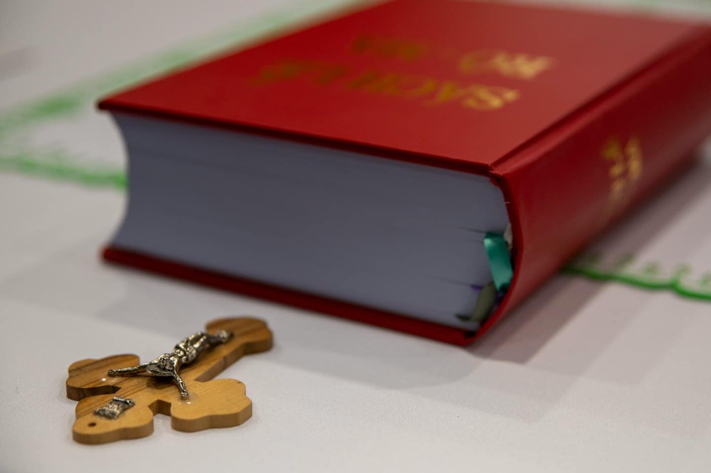 Un libro religioso con copertina rigida rossa e un crocifisso di legno su sfondo bianco.