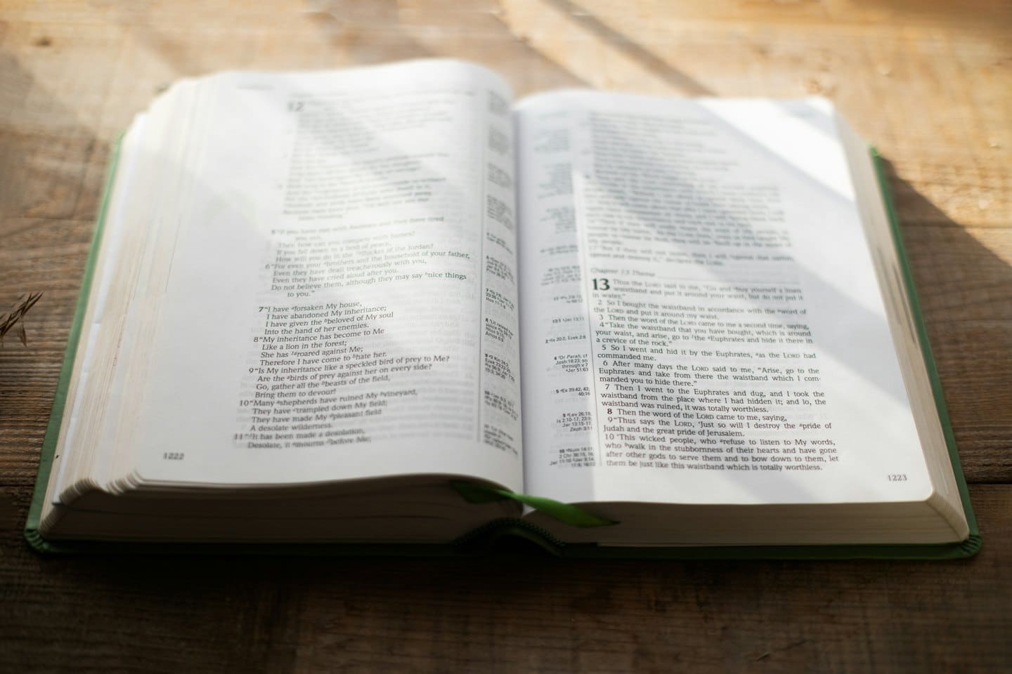 Bibbia rilegata in pelle aperta con segnalibro verde su un tavolo di legno.