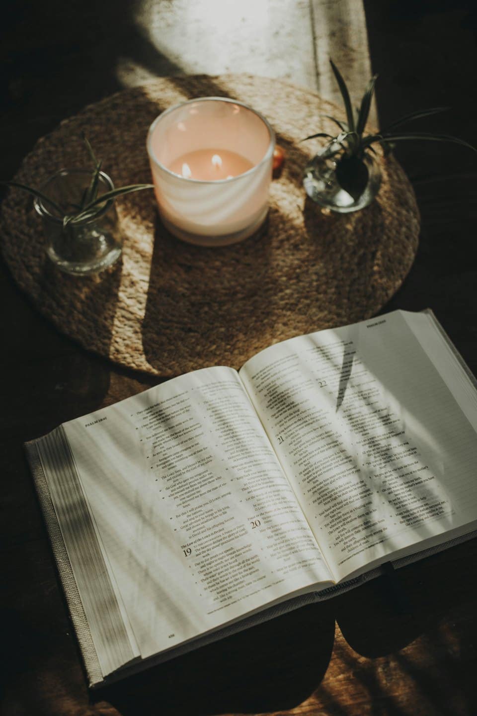 Bibbia aperta con candela e piante su un tavolo di legno.
