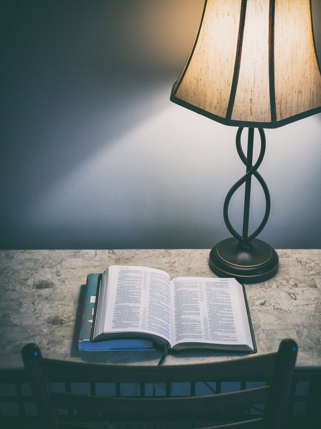 Una Bibbia aperta è appoggiata su libri accatastati accanto a una lampada.