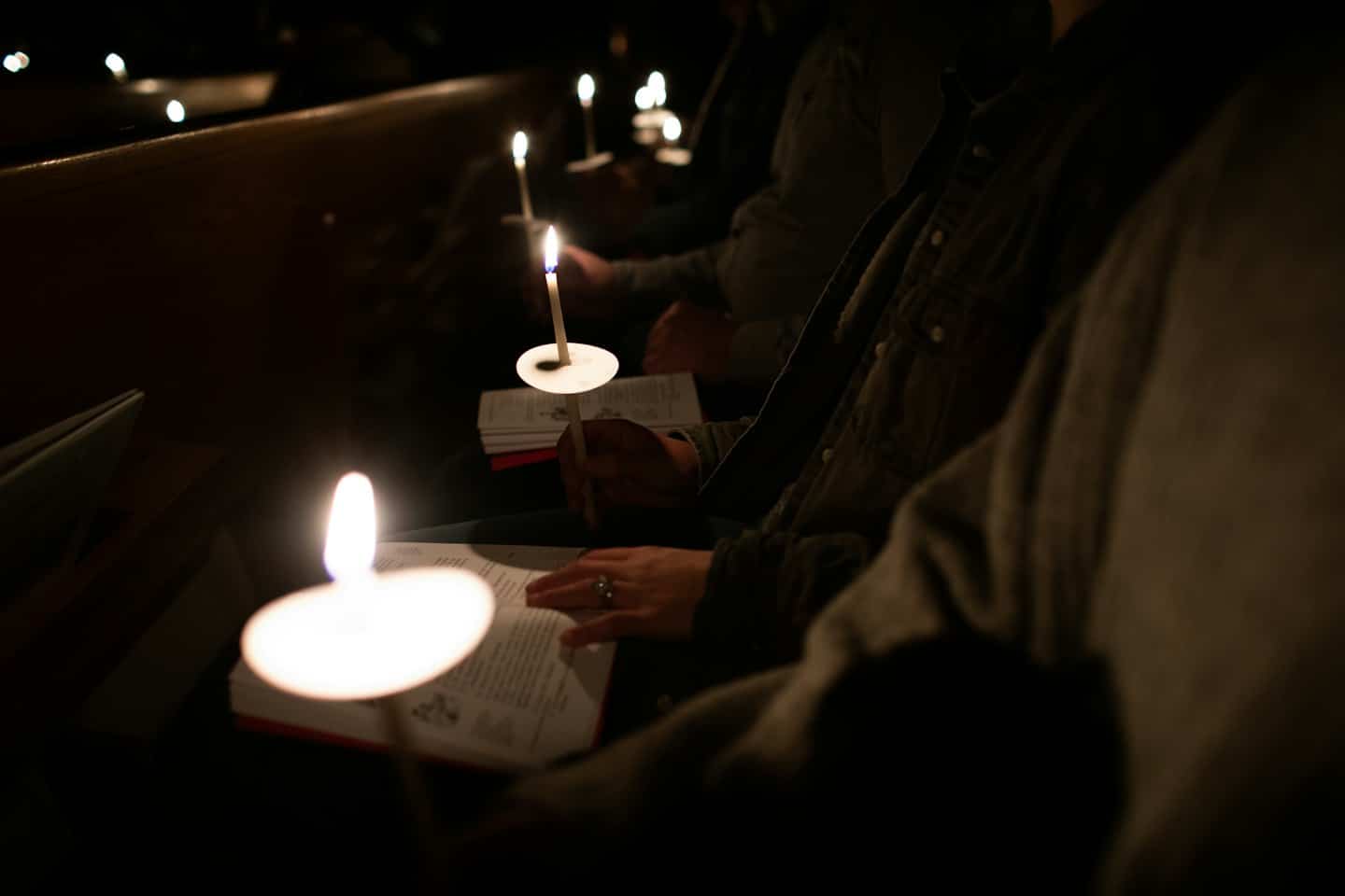 Mani che tengono una candela accesa e un libro aperto in chiesa.